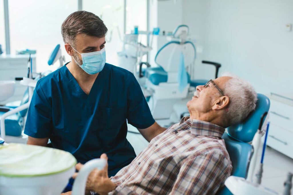 elderly man laying in dental chair talking with doctor
